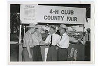 Four men at 4-H Club County Fair Booth (021-003-697)
