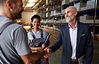 A white colar man shake hands with two workers at the storage house