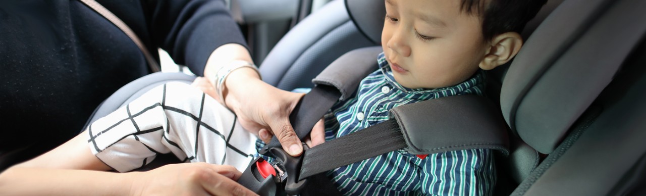 boy being buckled in child car seat