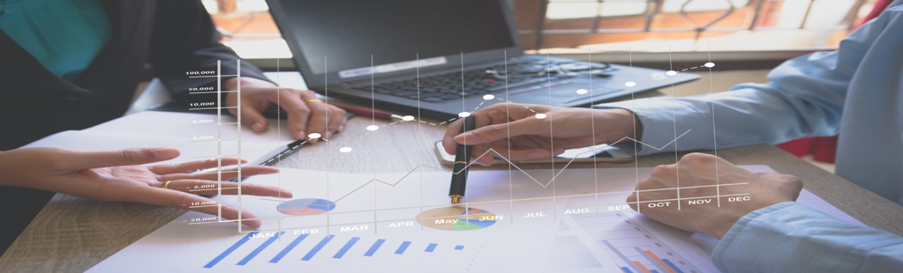 hands of two people discussing data on a table in front of them, open laptop in back, graph showing above paper graphs